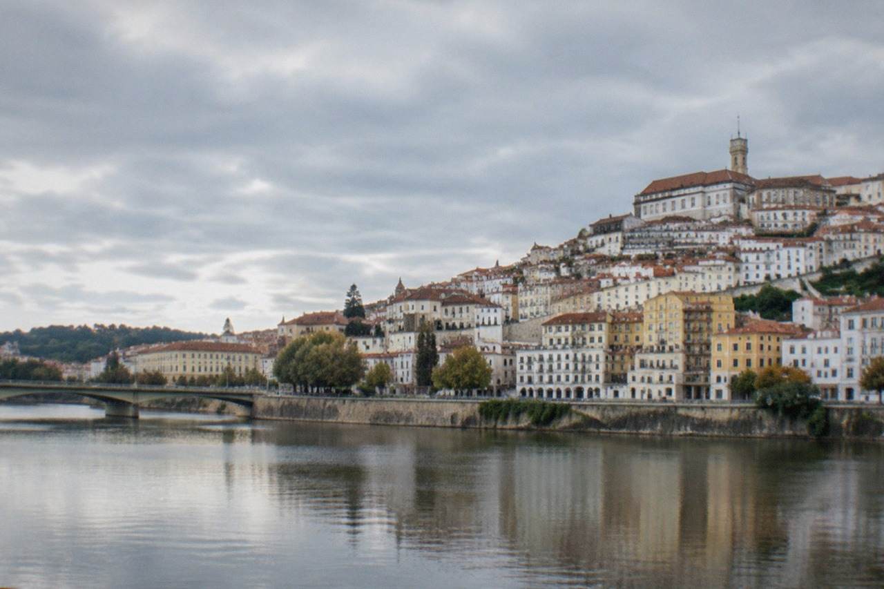 The old city of Coimbra in Portugal seen from across the River Mondego, with the university tower rising above the rooftops