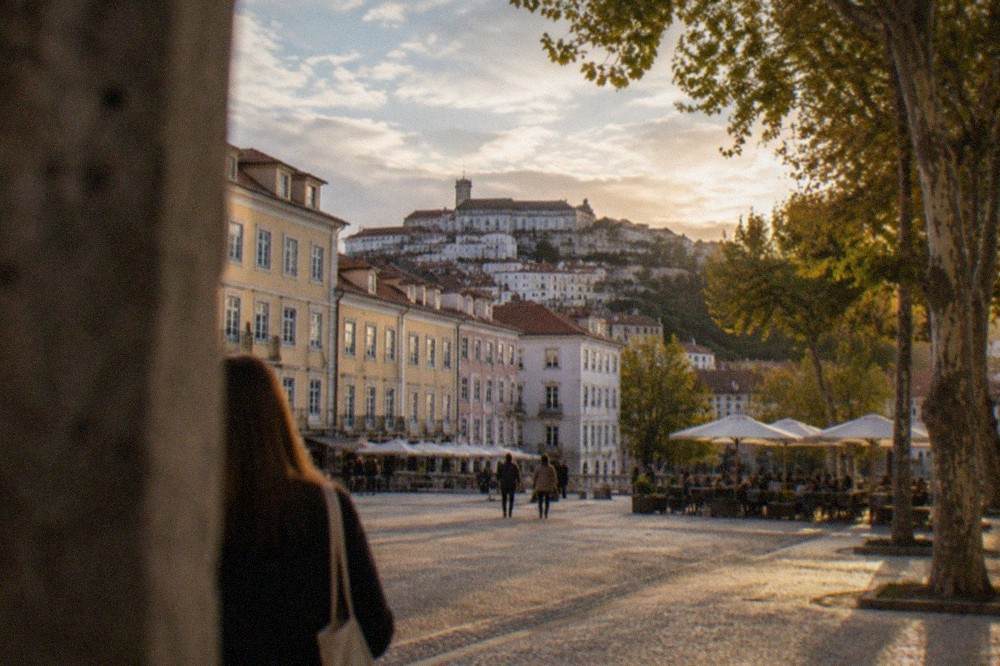 A cobbled lane in the old town of Coimbra, Portugal, with pastel-coloured buildings and the university hill rising behind the rooftops