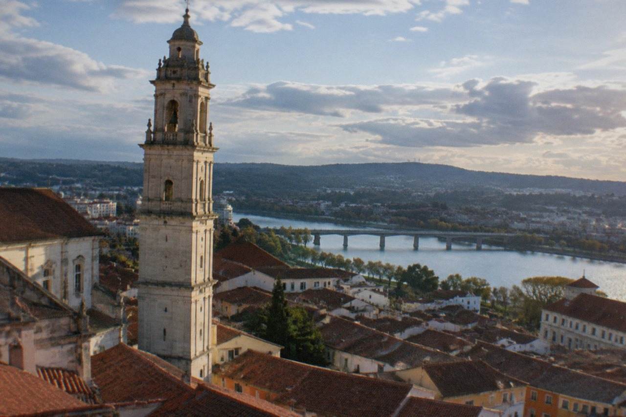View over the tiled roofs of Coimbra, Portugal, with the university tower rising above the old town and the River Mondego in the distance