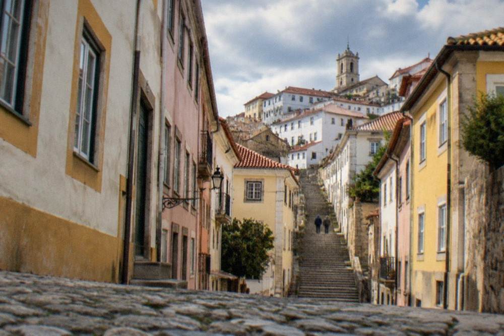 Cobbled street in Coimbra's old town with pastel-coloured buildings and the steep stairway up toward the university hill
