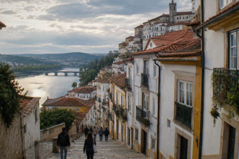 Visitors walking down a narrow old-town street in Coimbra towards the River Mondego