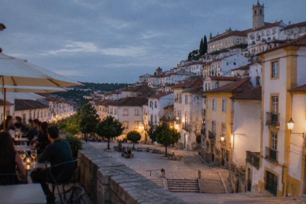 Diners at an outdoor table in a Coimbra square in the evening