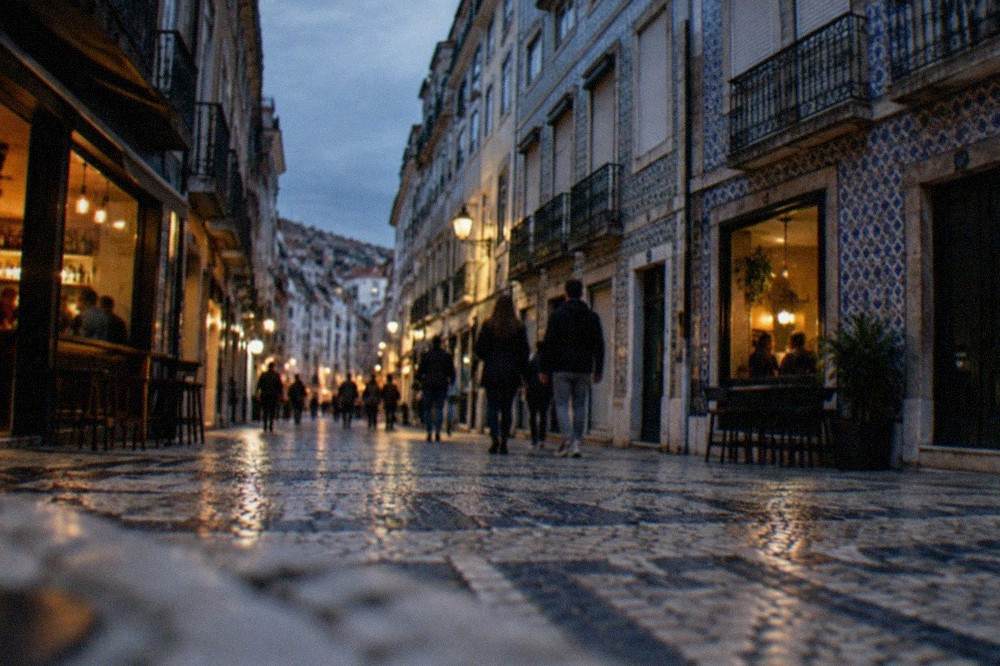A narrow street in the Baixa district of Coimbra at night with lit bar windows and people walking
