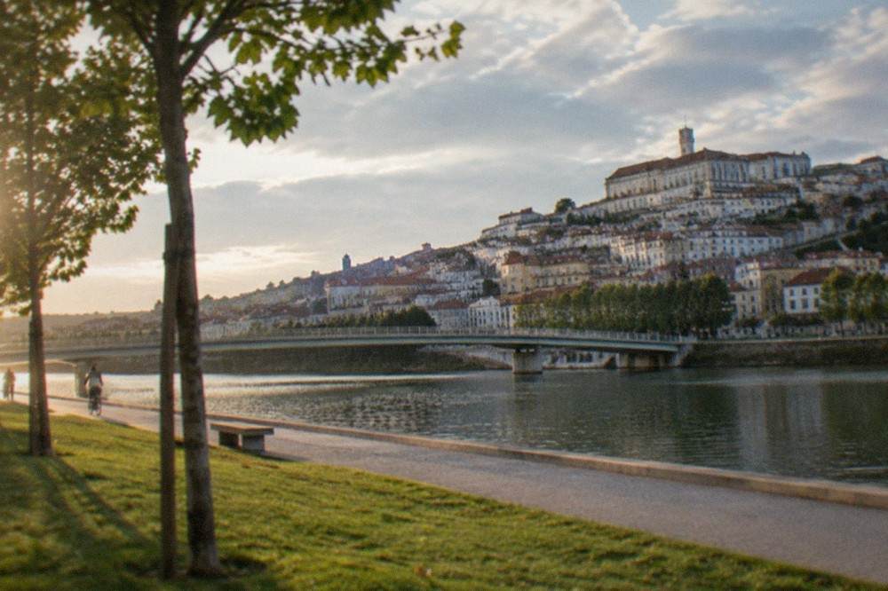 Riverside path along the Mondego with the old town and university buildings on the hillside above