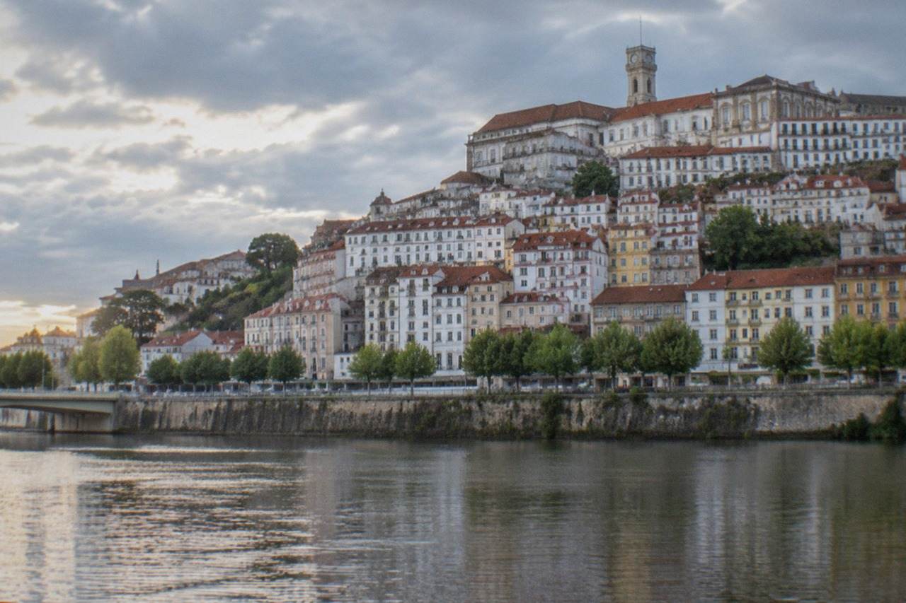 The old university buildings of Coimbra seen from below, with the River Mondego in the foreground