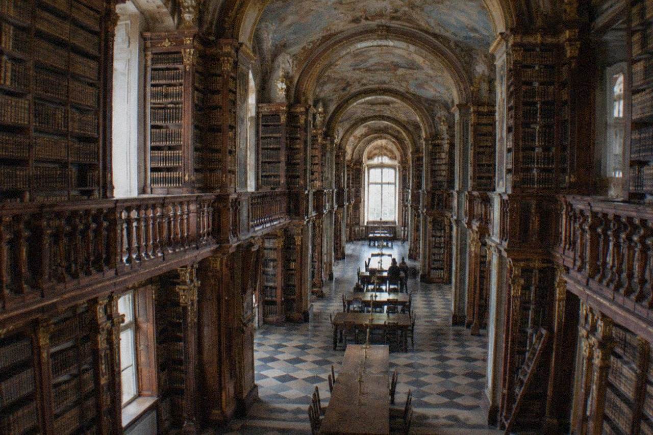 The grand baroque library hall of the University of Coimbra with tall bookshelves and painted ceilings