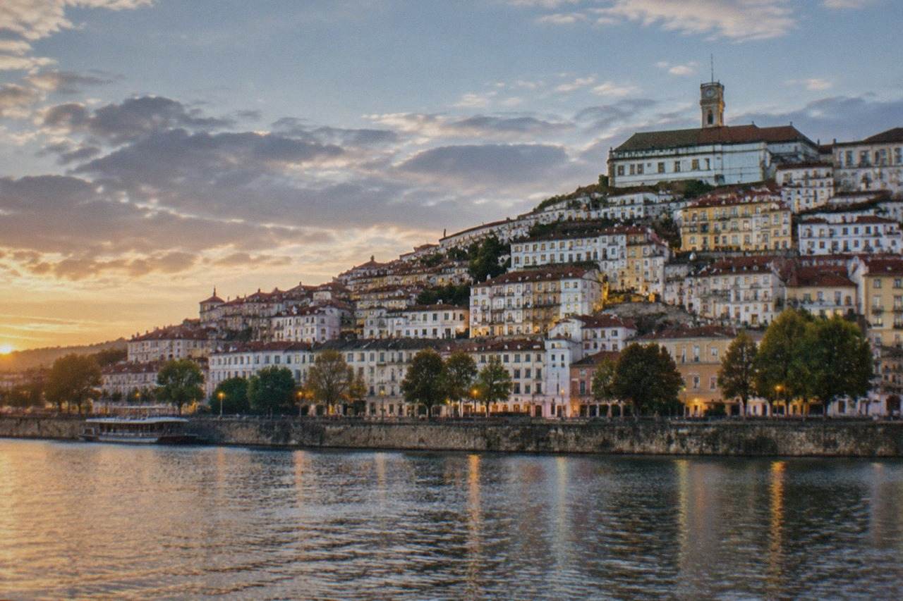 The lit windows and hillside buildings of Coimbra old town seen from across the River Mondego at dusk