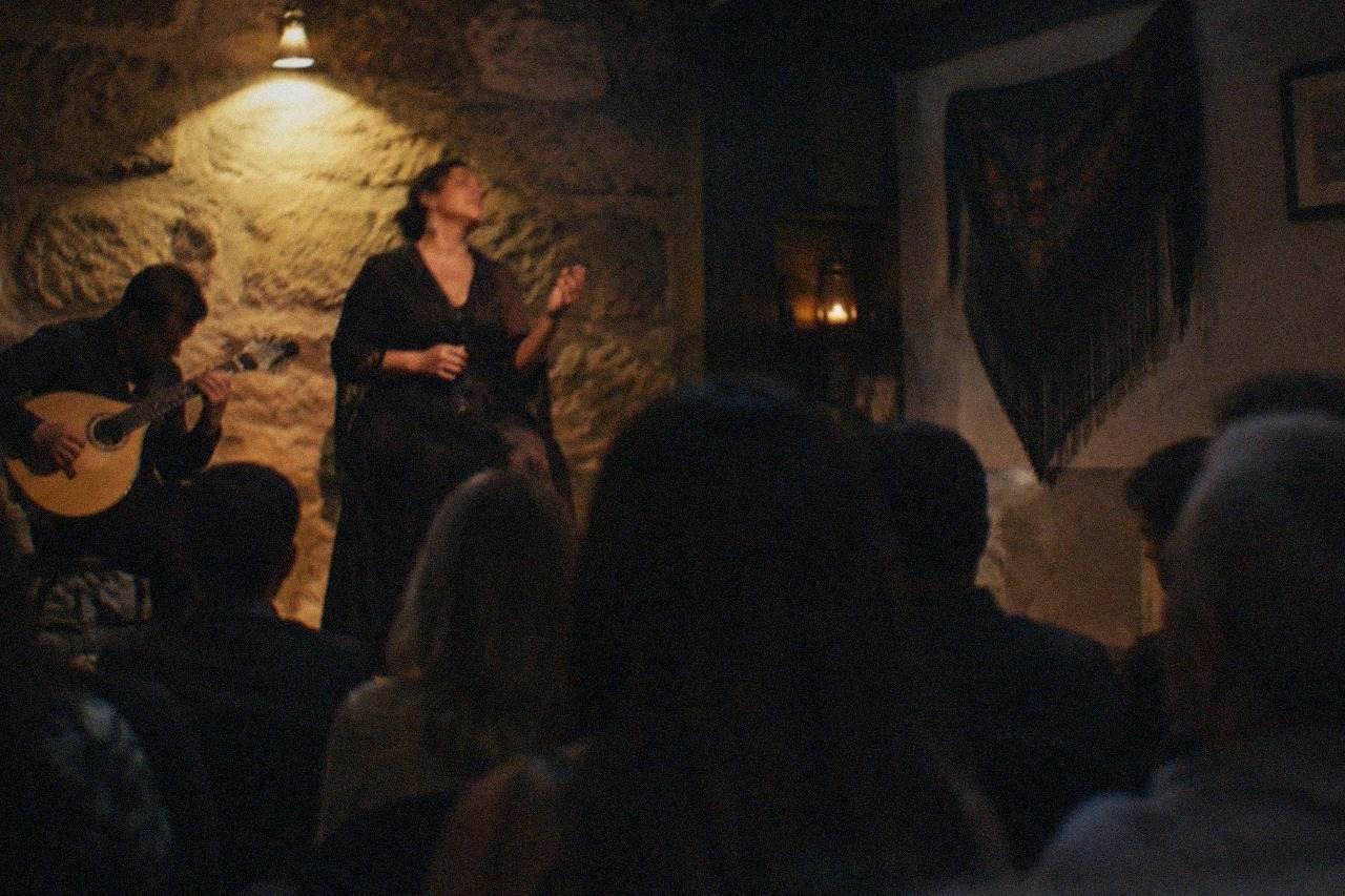 A singer in a dark traditional fado performance room with a guitar player beside her