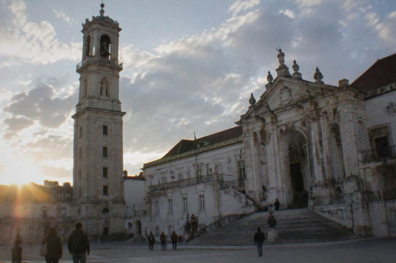 The grand baroque facade and clock tower of the University of Coimbra seen from the square below