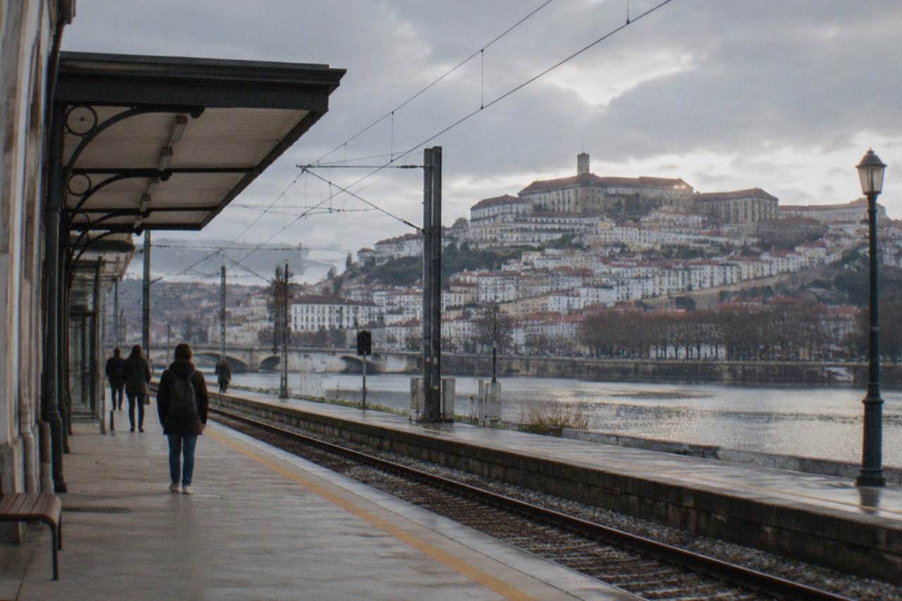 A railway platform in Coimbra, Portugal, with the old university city rising on the hill above the River Mondego in the background