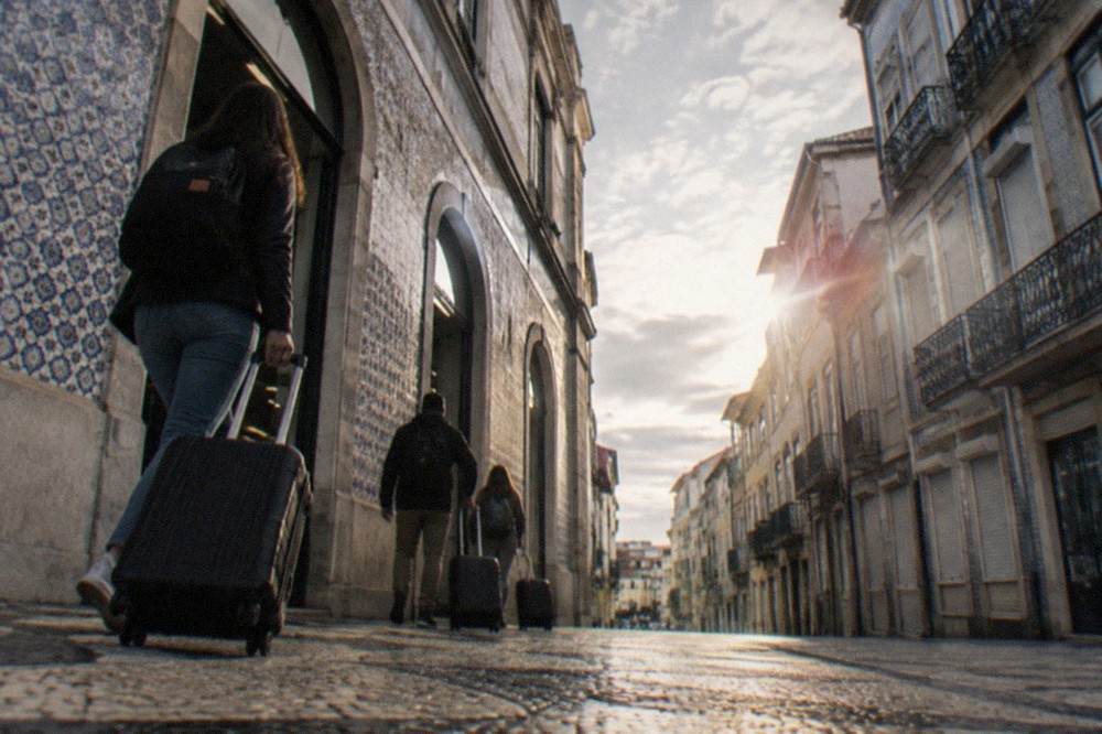 Travellers with luggage walking out of a railway station entrance in a Portuguese city, with tiled station walls and morning light
