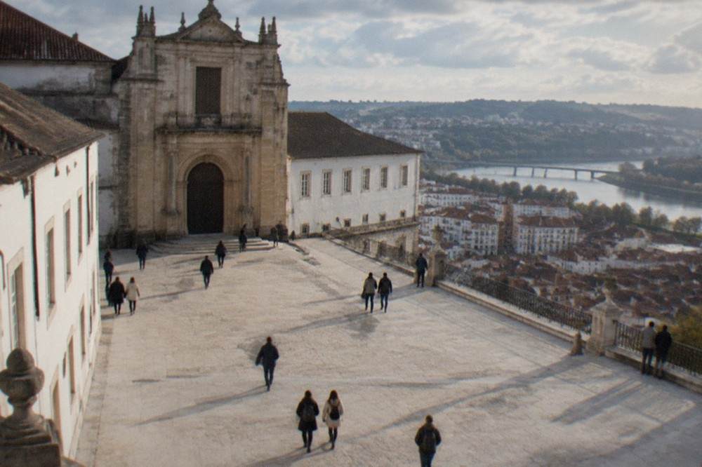 The stone courtyard and chapel facade of the University of Coimbra on the old royal hill, with visitors walking between the buildings.