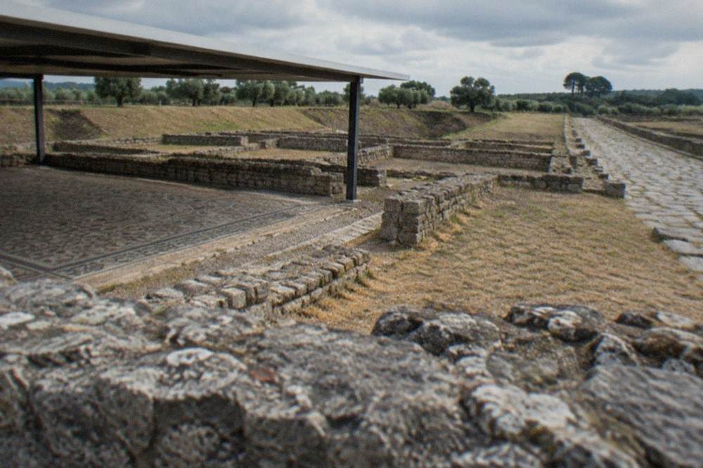 A stone-paved Roman road and low ruin walls at Conímbriga with trees beyond