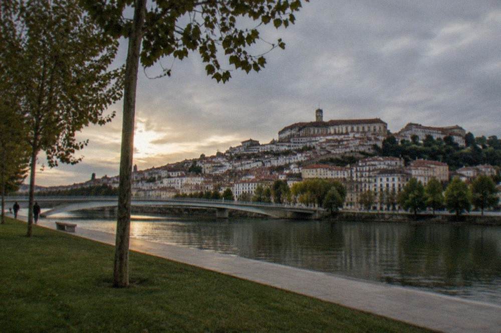 The Mondego riverside in Coimbra with the old town and university buildings rising above the water in evening light