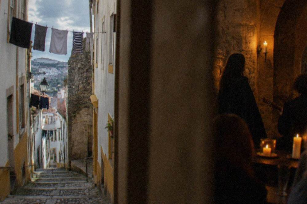 A student in a black academic cape singing fado in a candlelit stone room in Coimbra