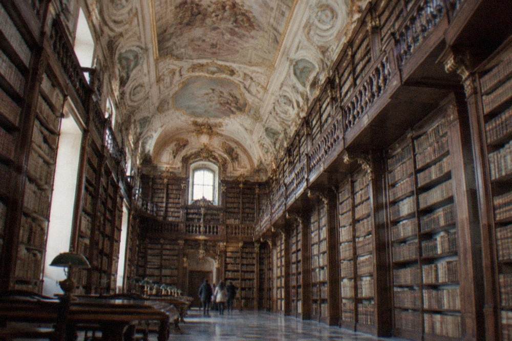 The baroque interior of a library with tall wooden bookshelves and painted ceilings