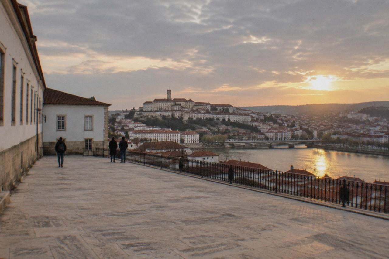 The University of Coimbra buildings and old town rooftops seen from across the River Mondego at golden hour