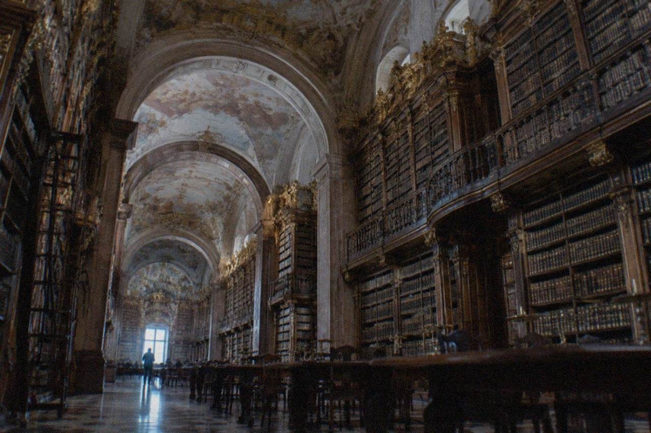 Ornate baroque library hall with tall wooden bookshelves, gilded decoration and painted ceilings