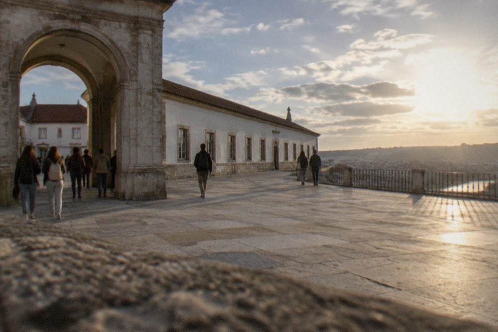 Students and visitors walking through the stone archway into the University of Coimbra's palace courtyard