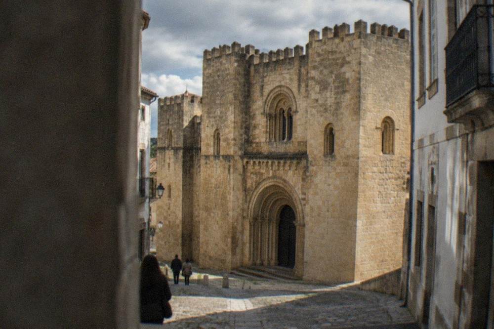 The Romanesque stone facade of the Sé Velha, the old cathedral of Coimbra, seen from a narrow lane