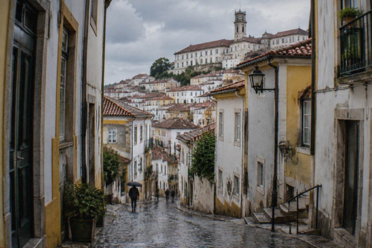 Rain-slicked cobblestone street in Coimbra's old town with the university tower visible above the rooftops