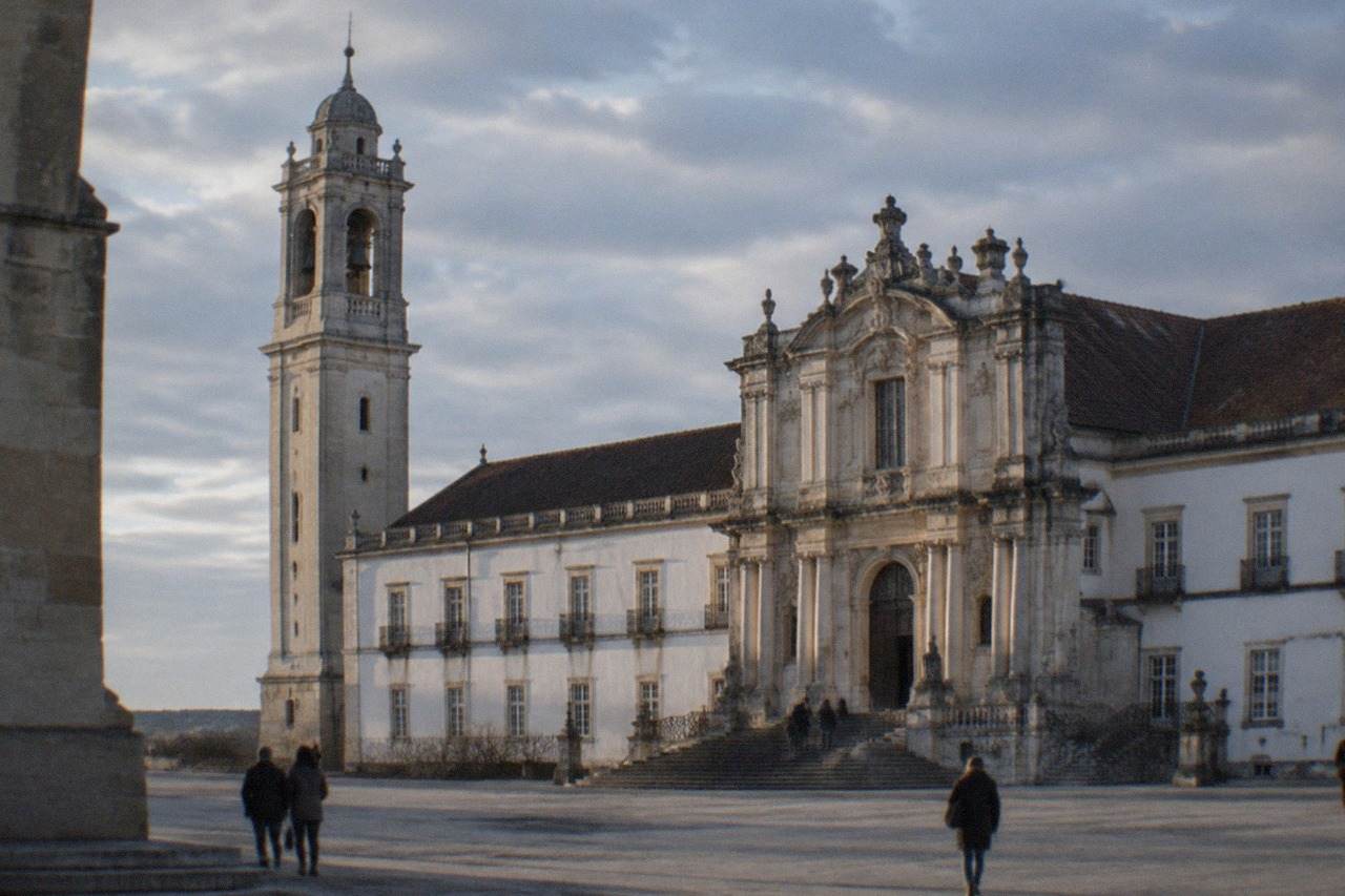 The grand baroque facade and clock tower of the University of Coimbra seen from the square below