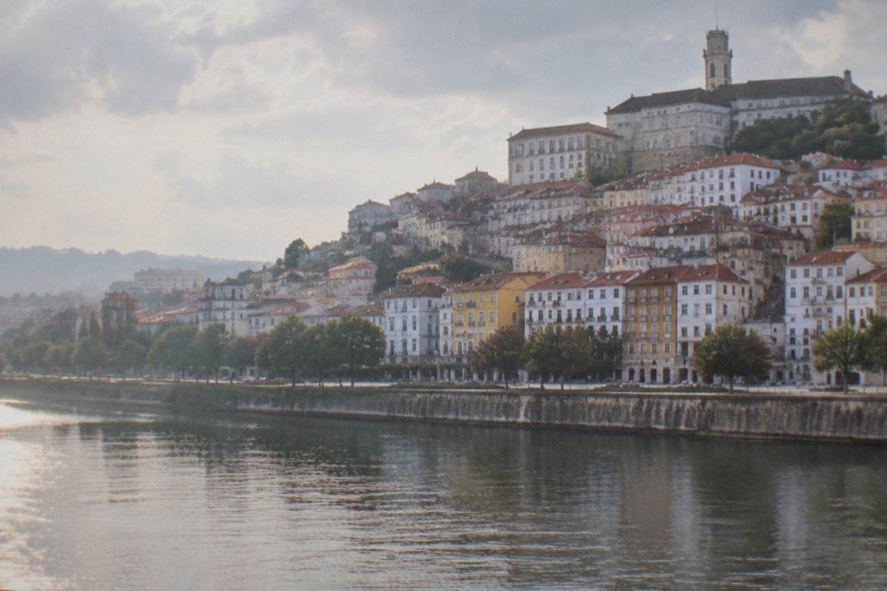The hillside of Coimbra seen from across the River Mondego, with the university tower rising above red rooftops.