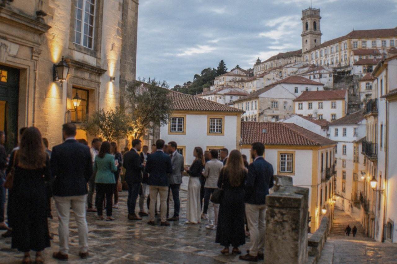 An evening crowd in smart casual clothing gathered outside a lit stone building in the old town of Coimbra