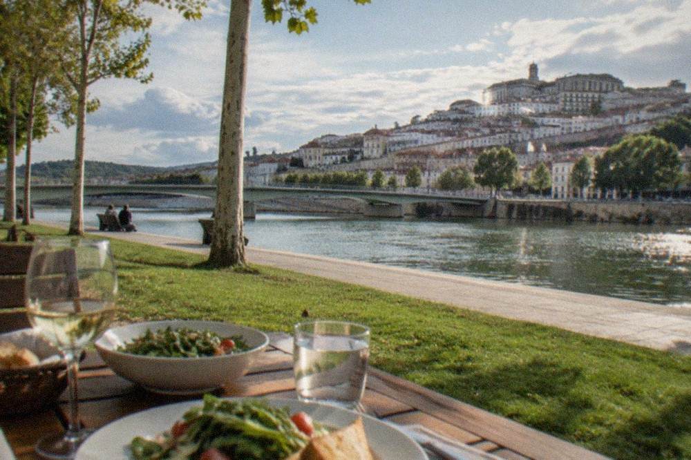 A dinner table beside the River Mondego with the lights of Coimbra's old town behind it