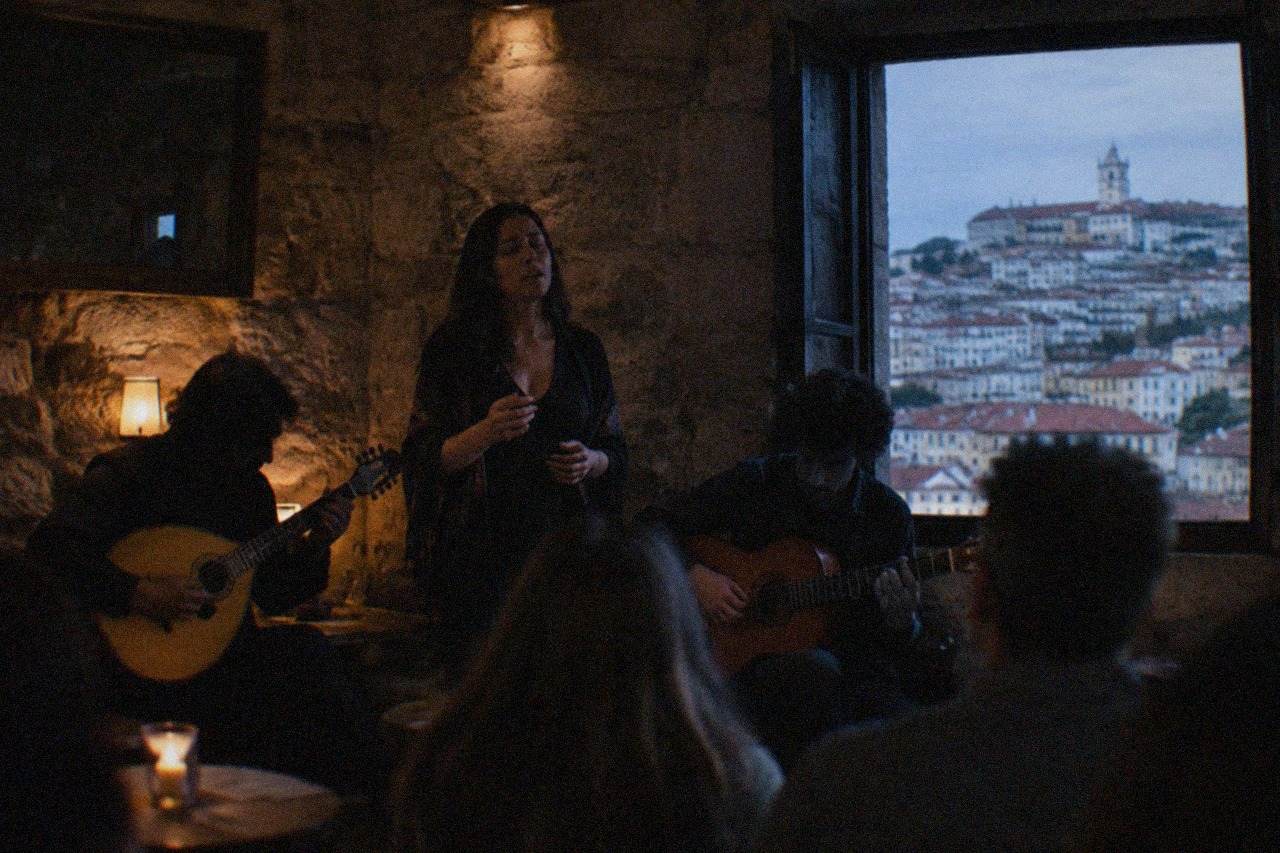 Two musicians playing Portuguese guitar and viola beside a singer in a dimly lit stone room in Coimbra