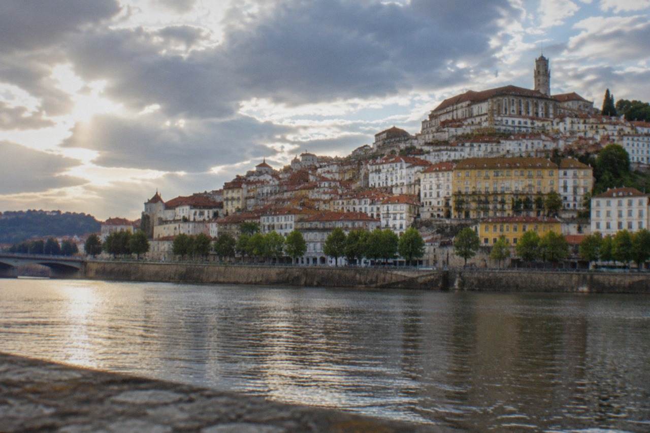 The old city of Coimbra in Portugal seen from across the River Mondego, with the university tower rising above red rooftops.