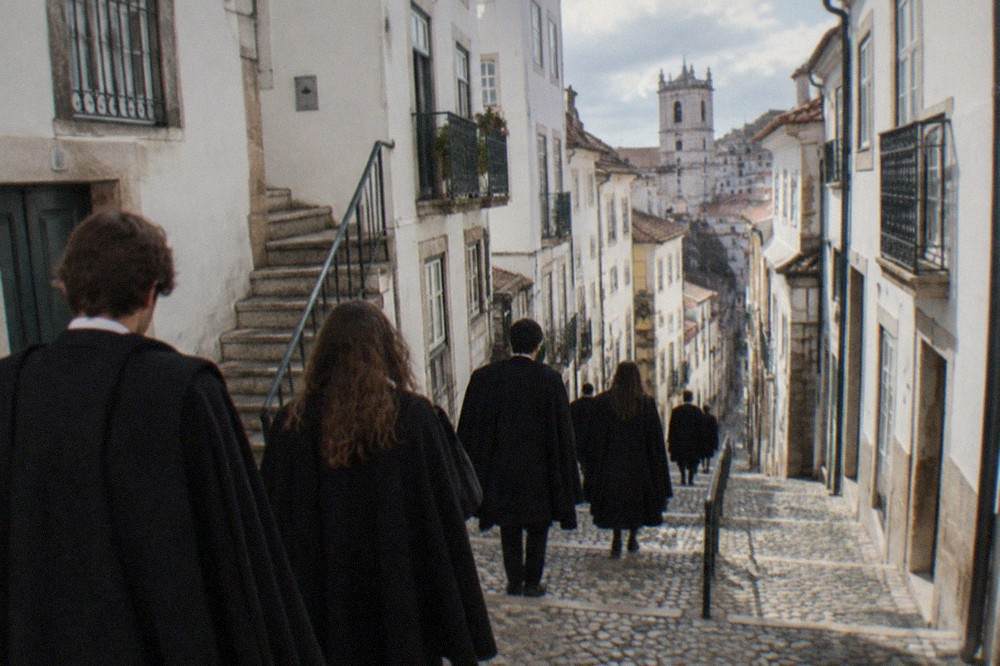 Students in black capes walking down a cobbled street in Coimbra's old upper town.