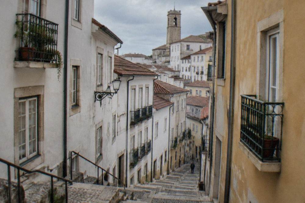 A narrow cobbled lane of Coimbra's old upper town with whitewashed and ochre walls in bright sunlight