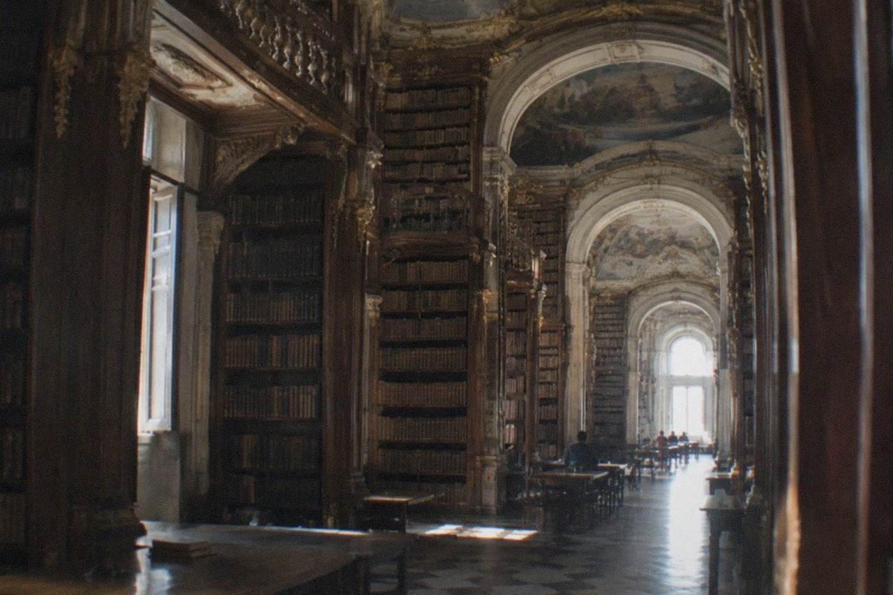 The ornate gilded reading room of a baroque library with tall wooden bookshelves and painted ceilings