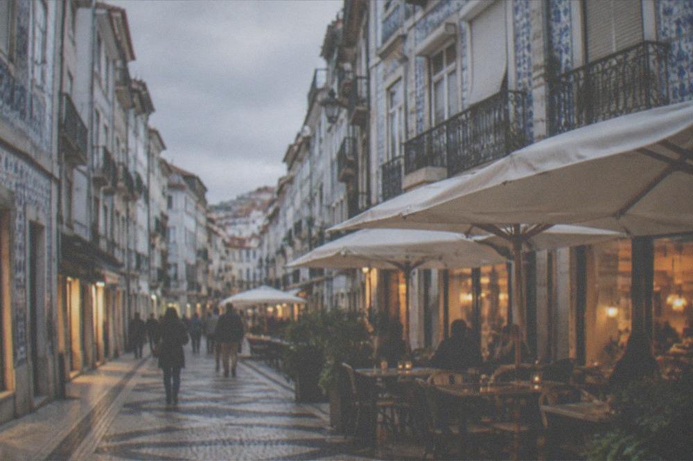 An evening food street in Coimbra's lower town with lit restaurant windows and outdoor tables