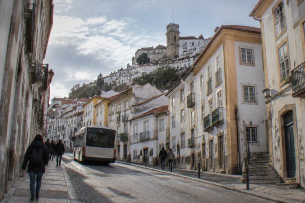 A city bus and pedestrians on a sunny street in central Coimbra