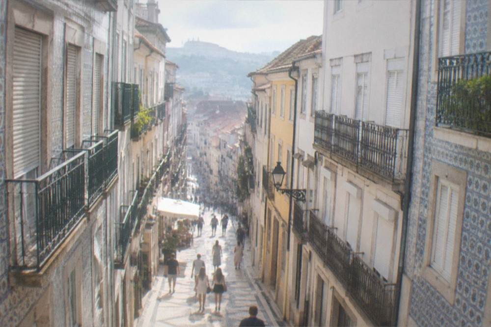 Visitors walking a sunlit cobbled lane between old buildings in Coimbra's lower town