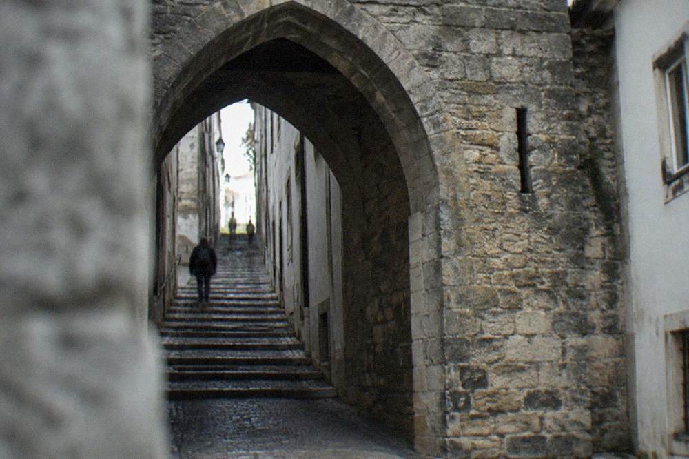 Stone archway of the Arco de Almedina leading into a narrow medieval street in Coimbra