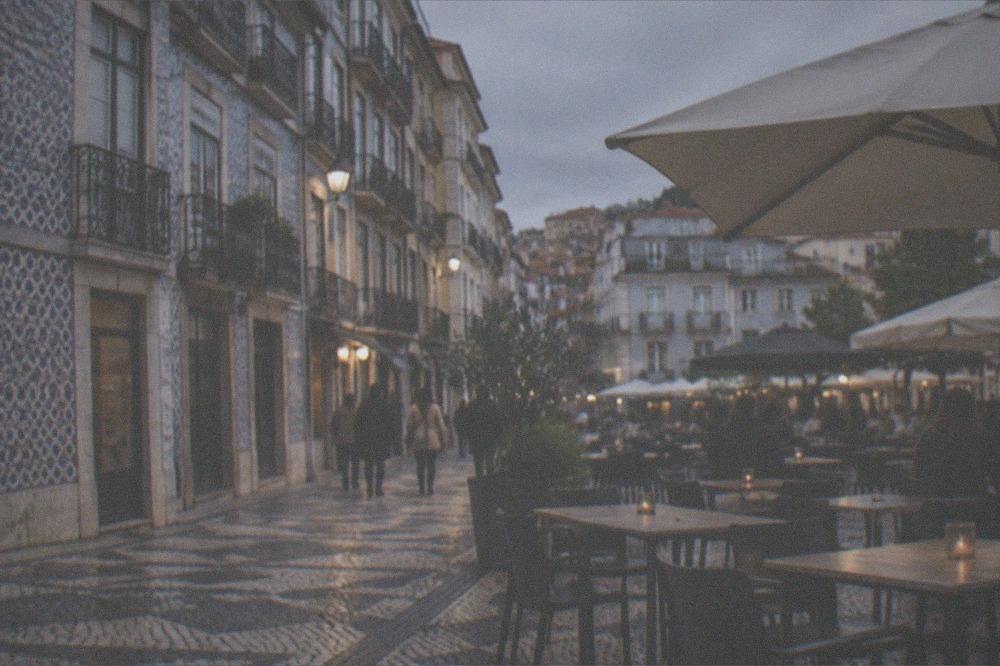 Outdoor tables of small restaurants on a paved square in Coimbra's lower town at dusk