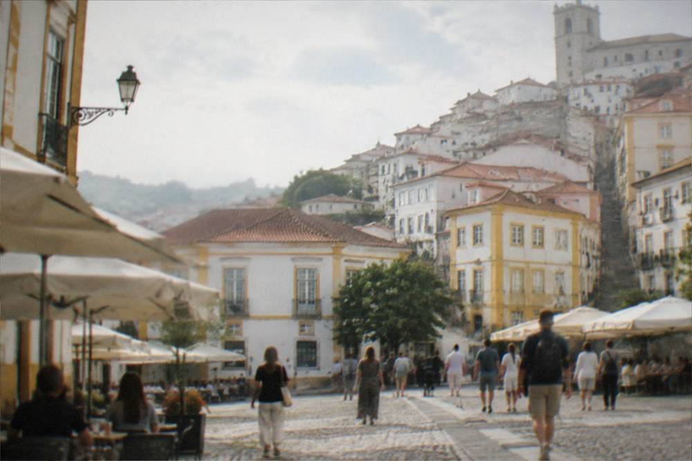 People walking across a cobbled square with cafe umbrellas in central Coimbra