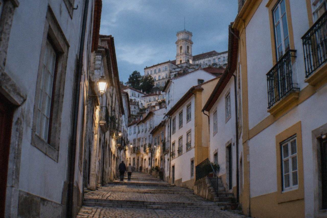 Narrow cobbled street in the old town of Coimbra with old stone buildings rising toward the university hill