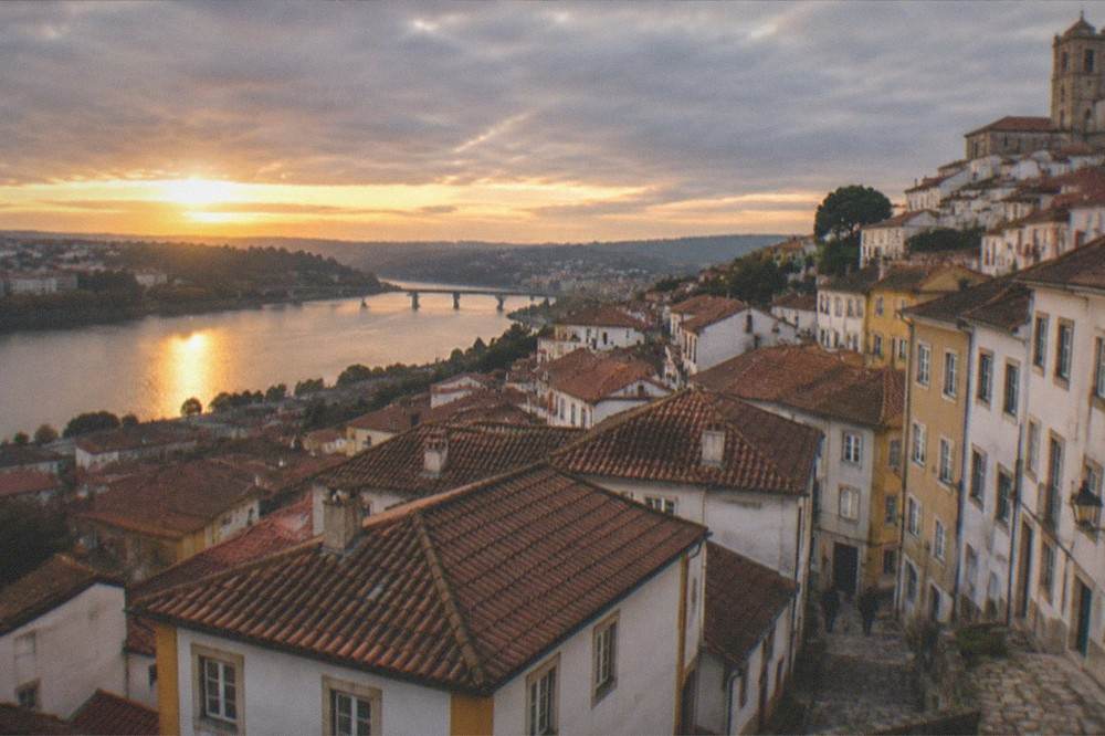 Wide view over the rooftops of the old town of Coimbra toward the river at golden hour