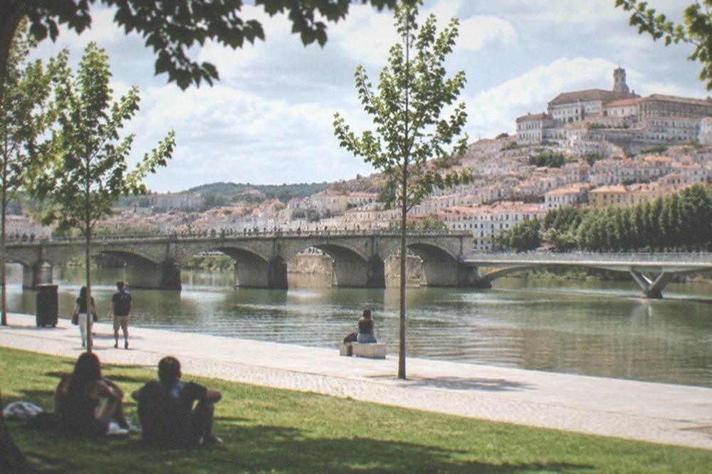 An old stone bridge over the Mondego with people walking across toward the flat Santa Clara side