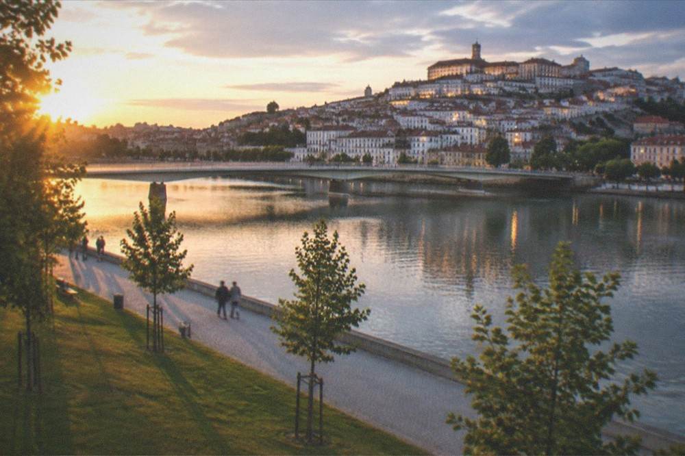 The arched bridge over the Mondego at dusk with the illuminated old town and university buildings reflected in the river