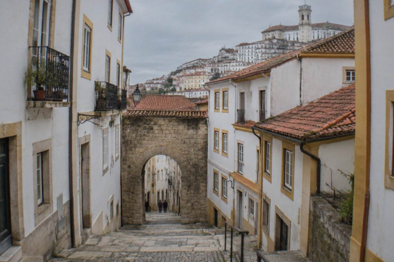 An old stone arched gateway in a narrow street in Coimbra, with buildings rising on both sides