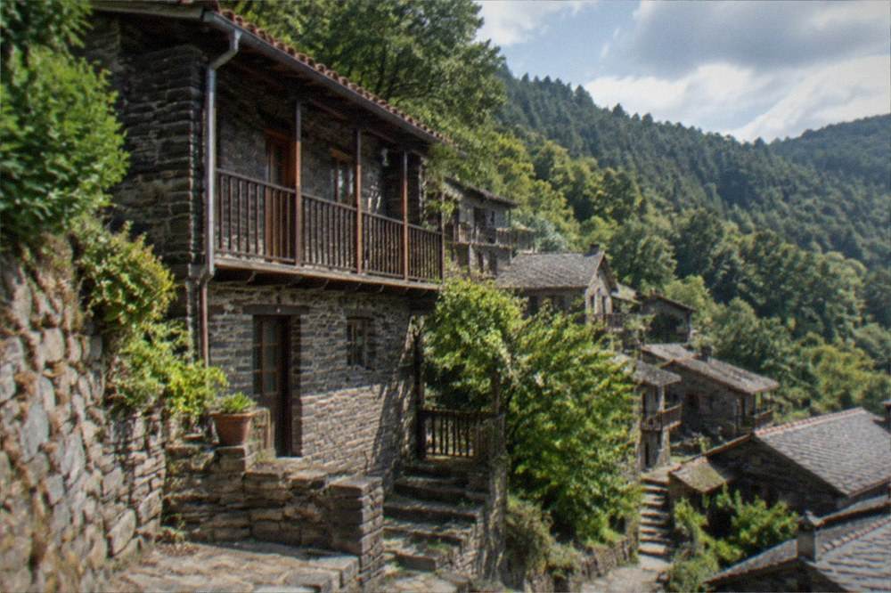 A stone schist village house with wooden balconies on a forested mountainside