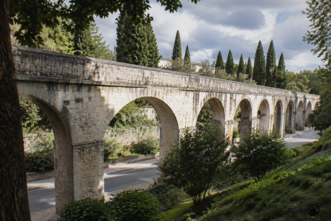 Stone arches of an old aqueduct rising over a green garden slope in Coimbra