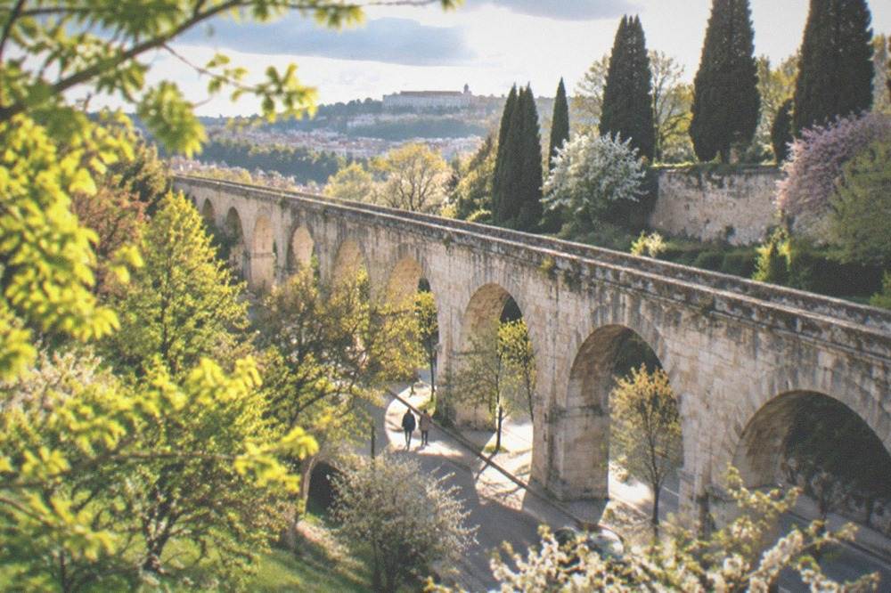 Aqueduct arches in Coimbra seen through spring greenery on a bright morning