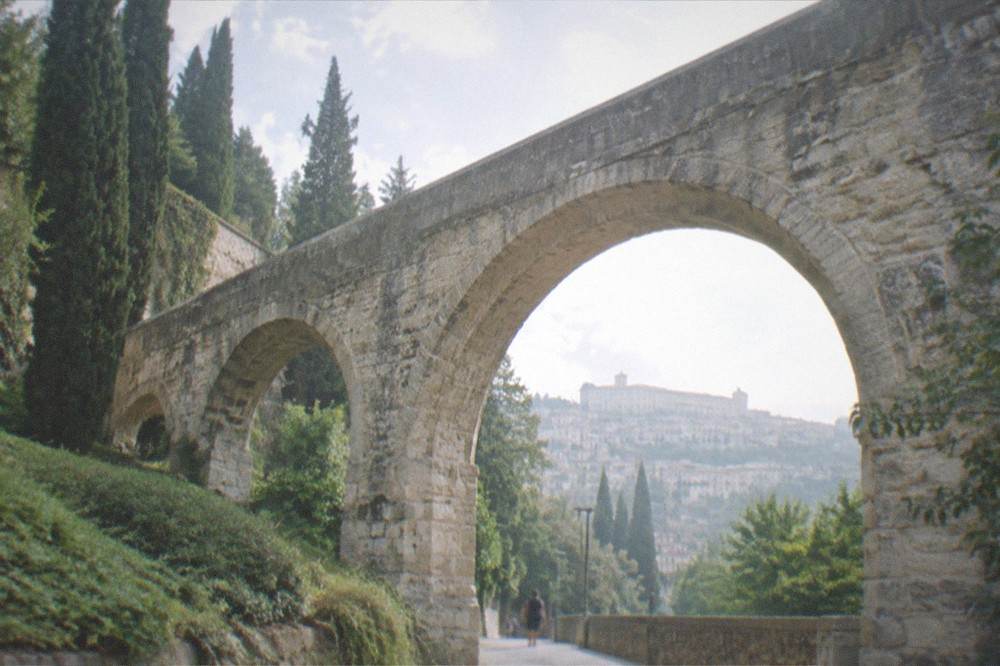 A stone aqueduct arch spanning a quiet garden path with the city hillside behind it