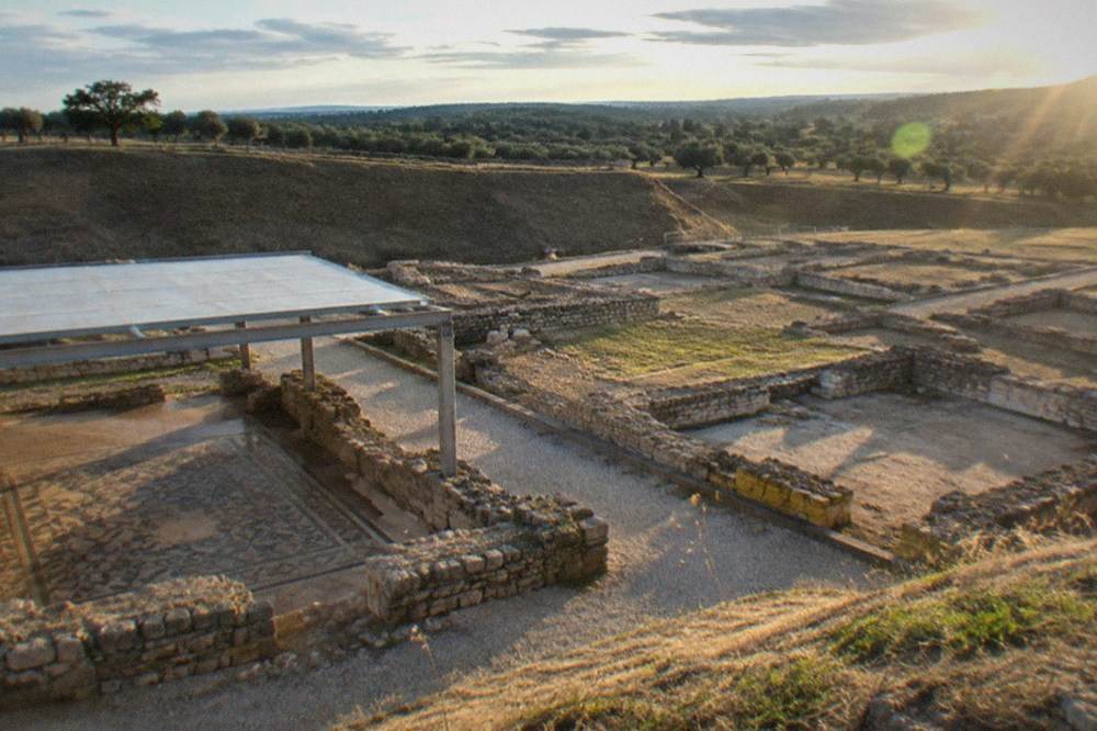 Late afternoon light across low stone walls and gravel paths of an excavated Roman town